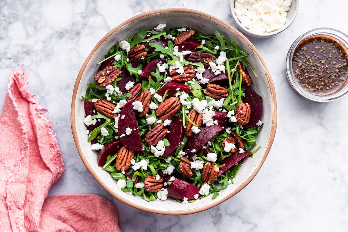A beet salad with arugula, pecans, and crumbled feta in a bowl.