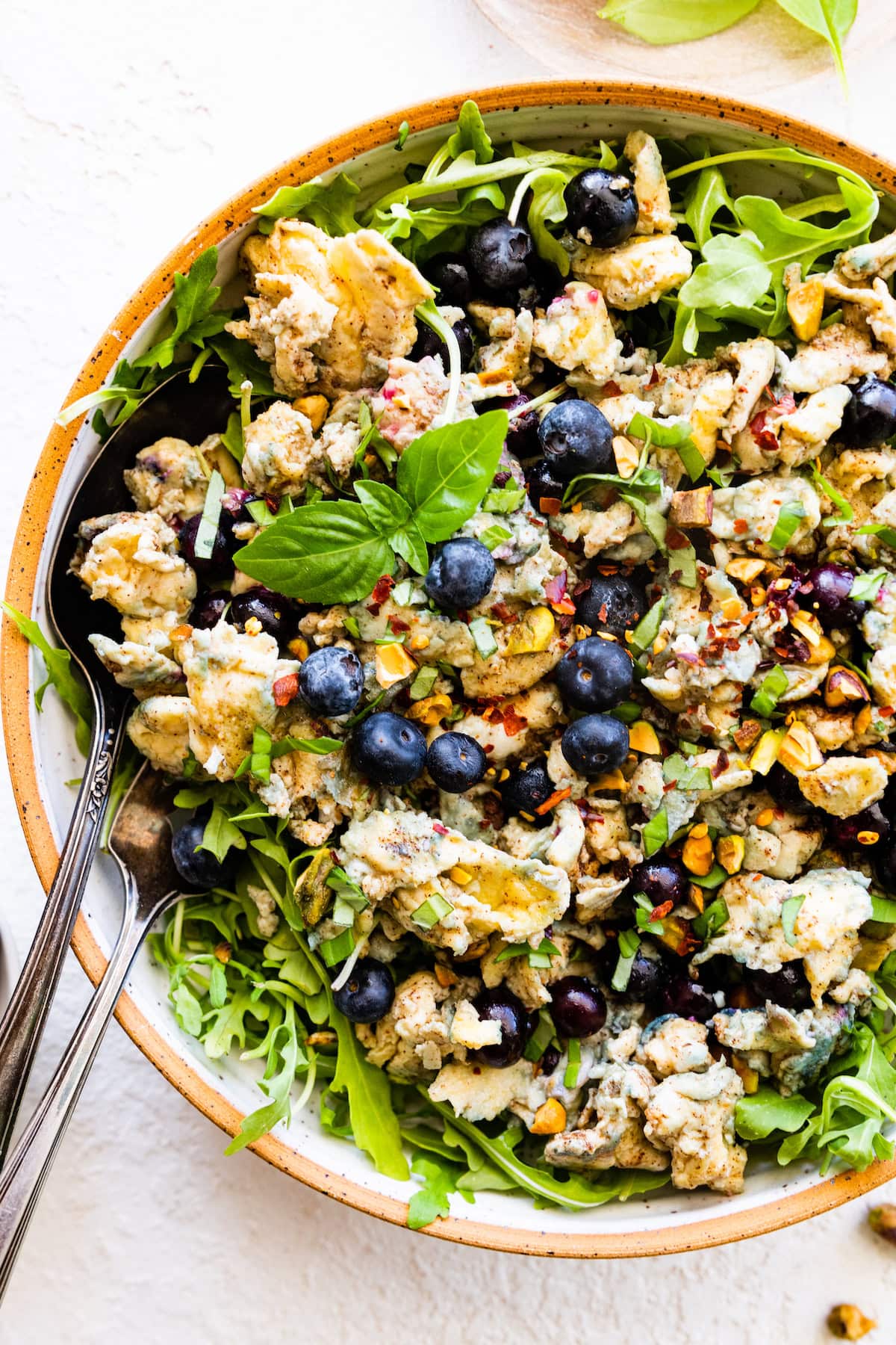 A large bowl with scrambled eggs, fresh blueberries, herbs, spices, arugula, and fresh basil leaves.