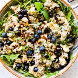 A large bowl of blueberry breakfast salad with scrambled eggs, fresh blueberries, arugula, herbs, and spices.