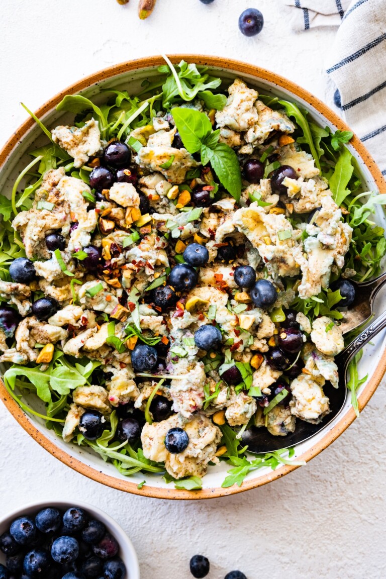A large bowl of blueberry breakfast salad with scrambled eggs, fresh blueberries, arugula, herbs, and spices.
