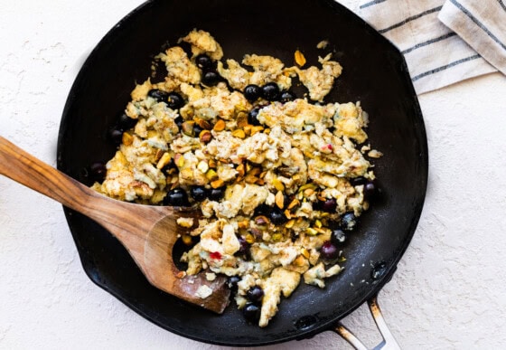 Cooked eggs with pistachios and blueberries in a skillet.