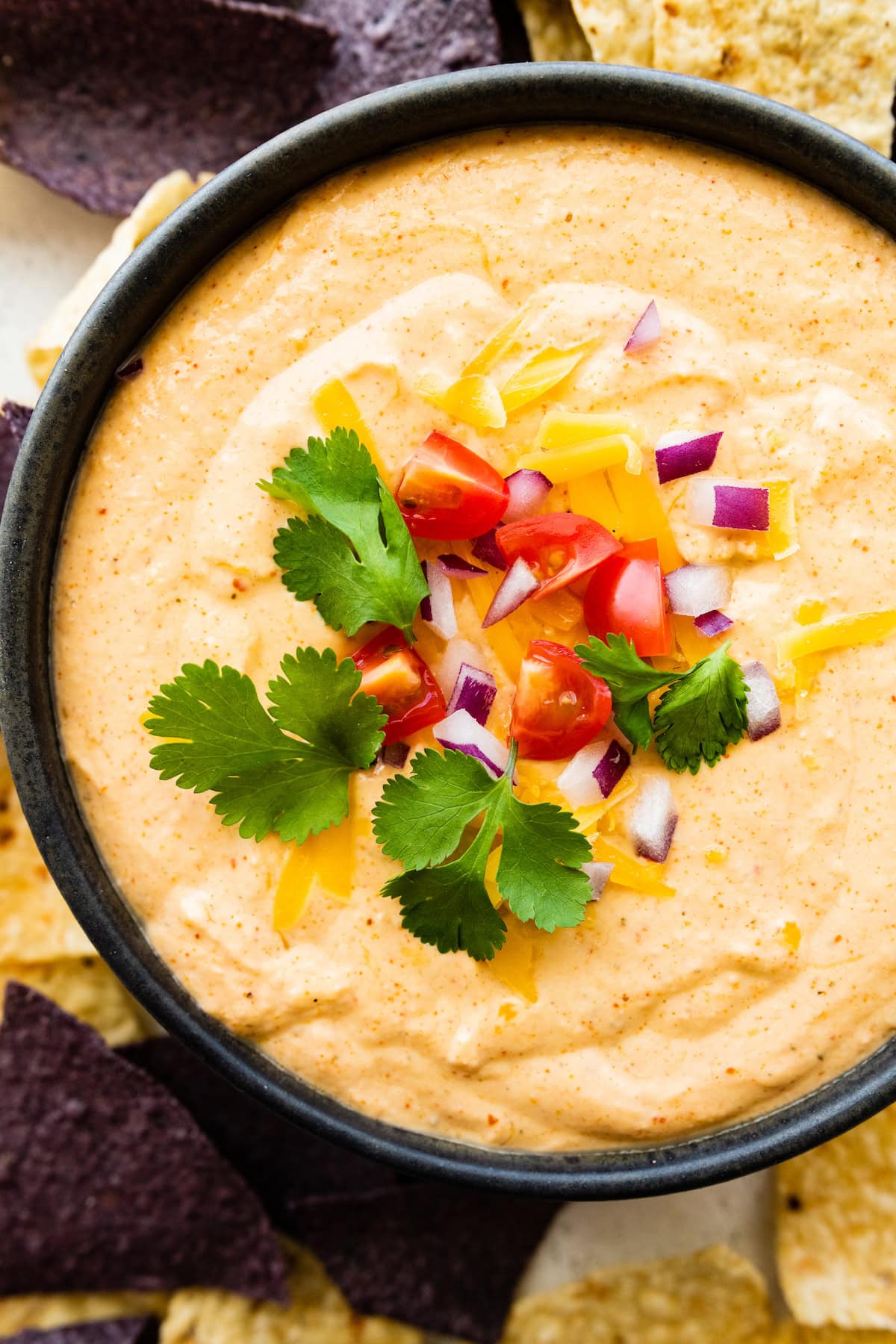 A serving of cottage cheese queso in a bowl topped with fresh cilantro, diced tomato, and red onion with tortilla chips on the side.