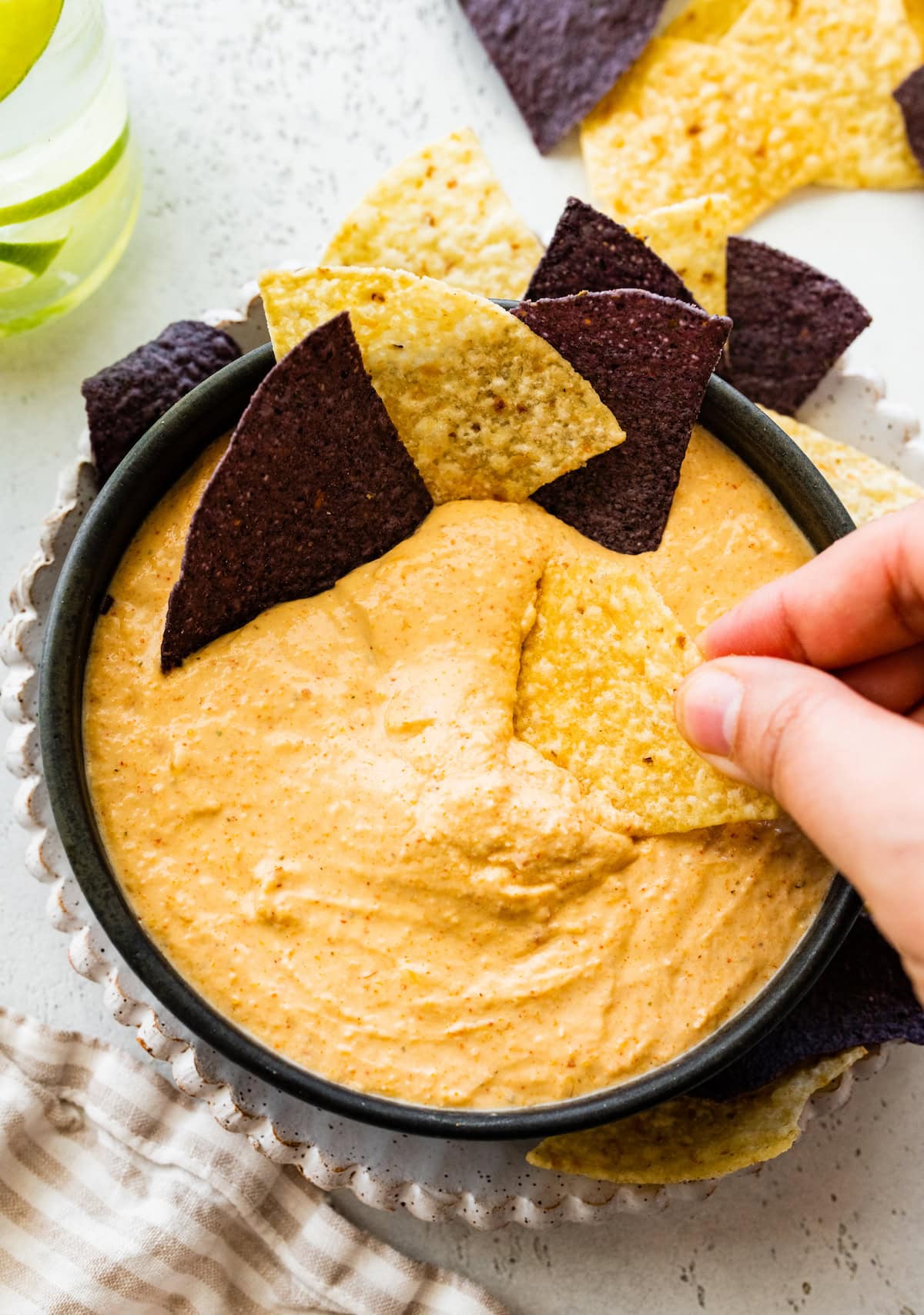 A womans hand dips a tortilla chip in a bowl of cottage cheese queso with more chips on the side.