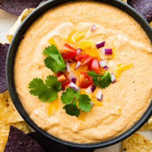 Cottage cheese queso served in a small bowl garnished with fresh cilantro, diced tomato, and red onion.