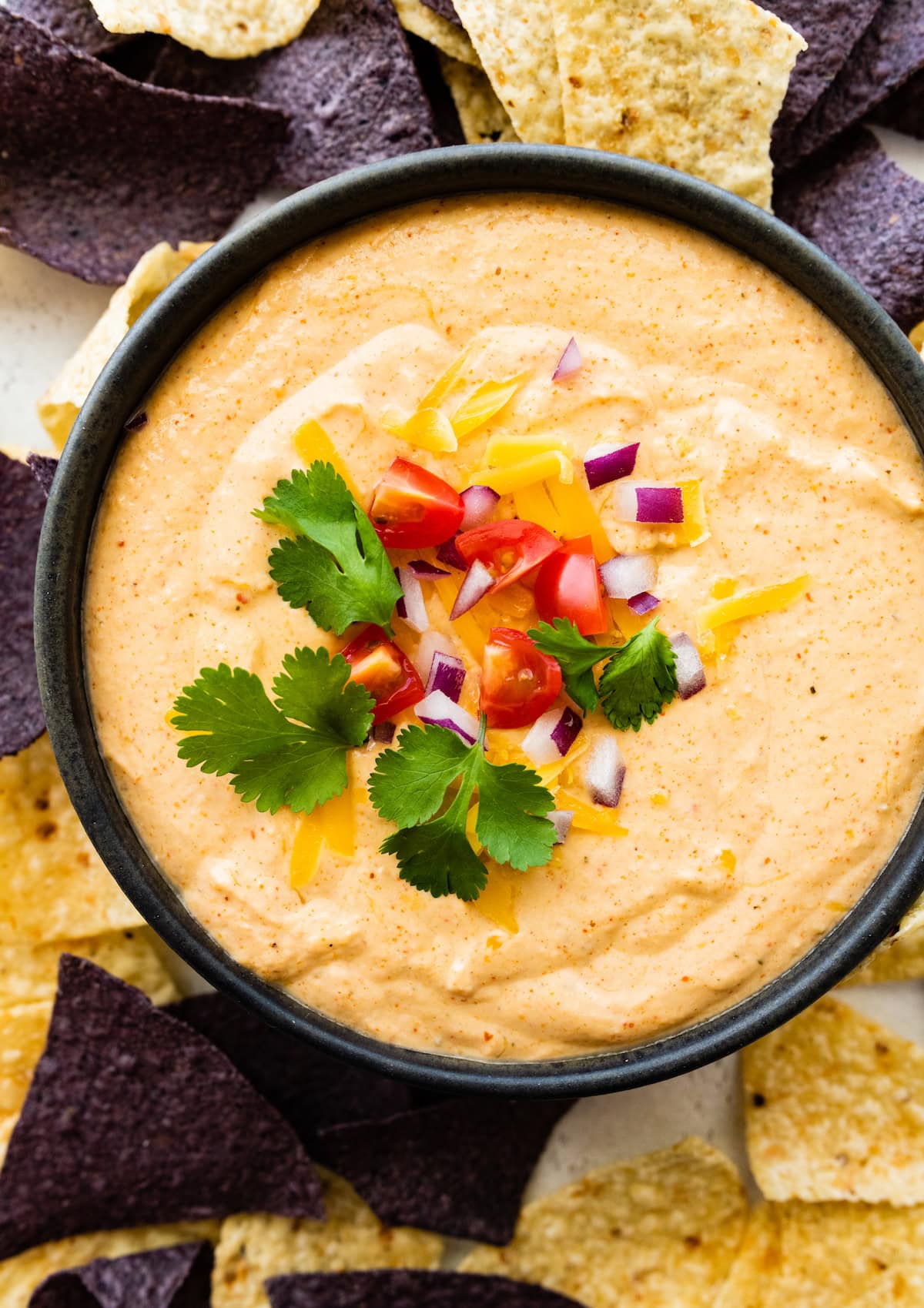 Cottage cheese queso served in a small bowl garnished with fresh cilantro, diced tomato, and red onion.