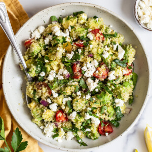 A serving of quinoa salad in a bowl with feta cheese, cherry tomatoes, and spinach.