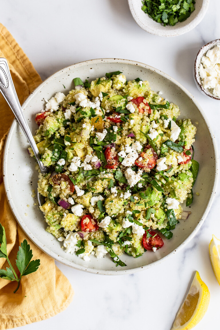 A serving of quinoa salad in a bowl with feta cheese, cherry tomatoes, and spinach.