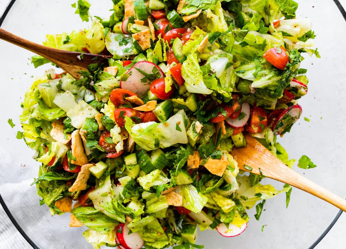 A large glass bowl of fattoush salad with two wooden serving spoons.