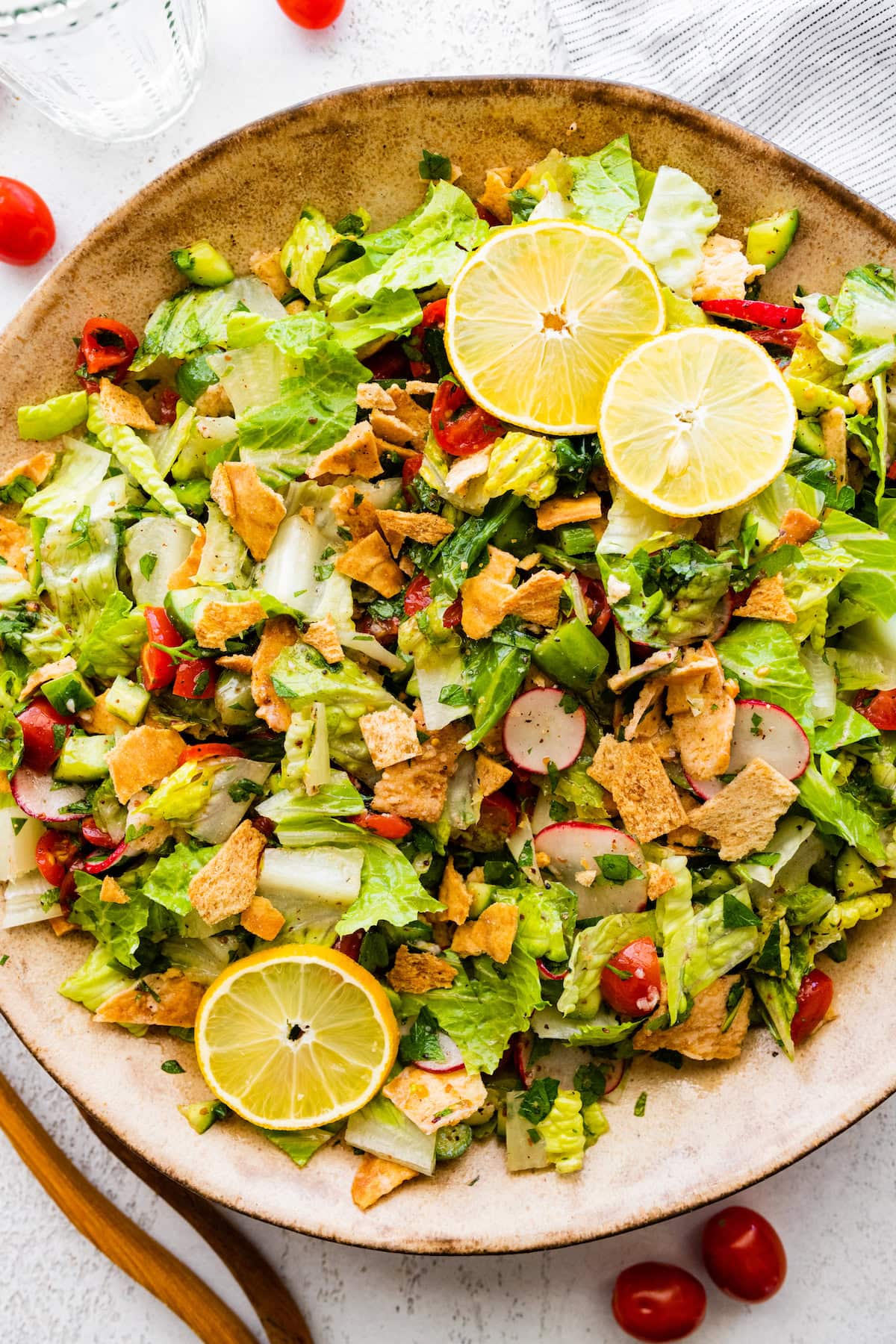 A large bowl of fattoush salad with ingredients like radishes, tomatoes, lettuce, pita chips, and lemon slices as a garnish.
