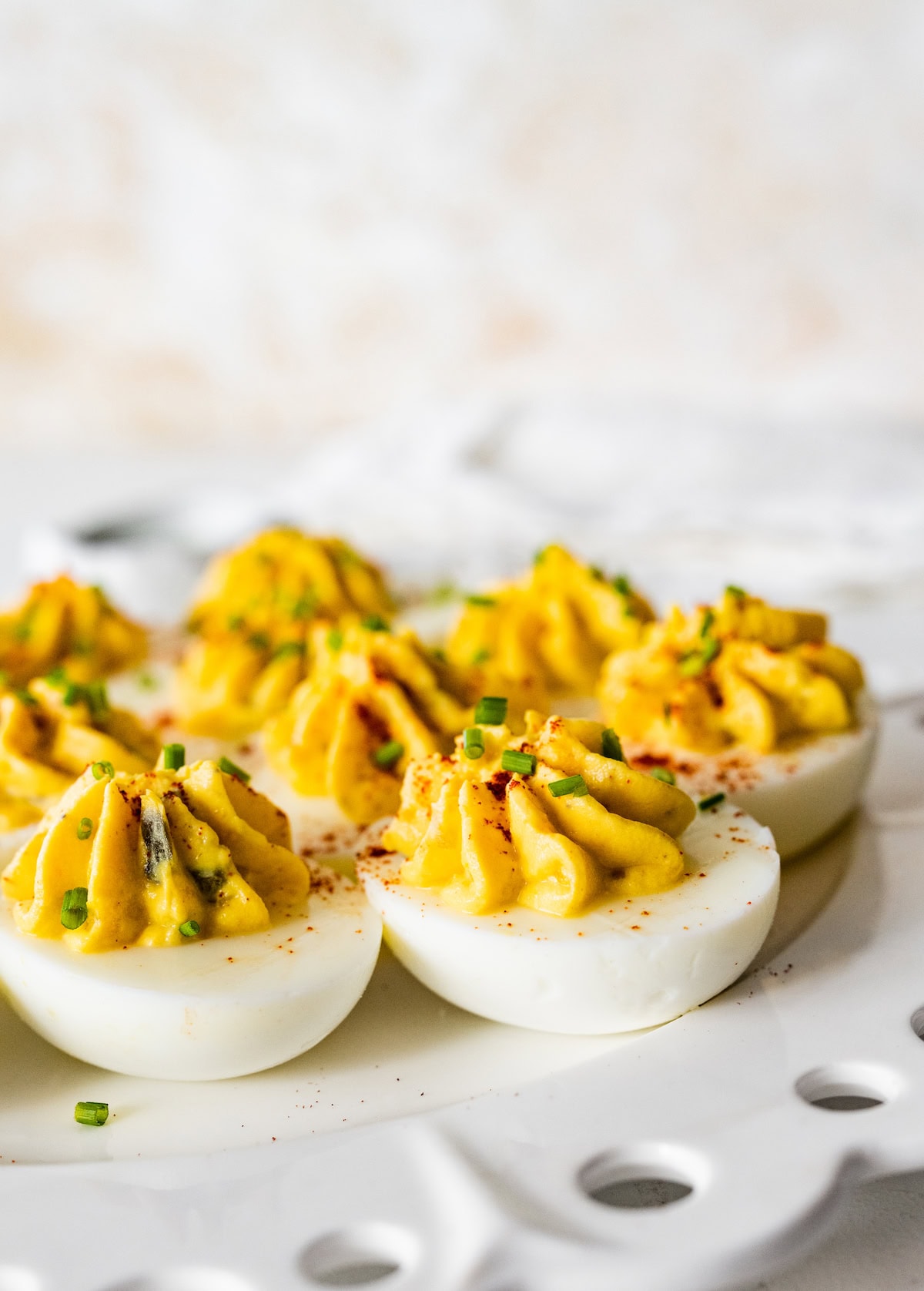 Deviled eggs served on a plate and topped with fresh chives and paprika.