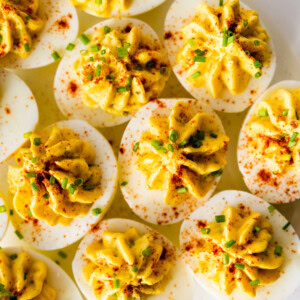 Deviled eggs topped with fresh chives, and paprika on a plate.