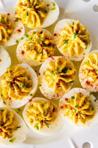 Deviled eggs topped with fresh chives, and paprika on a plate.
