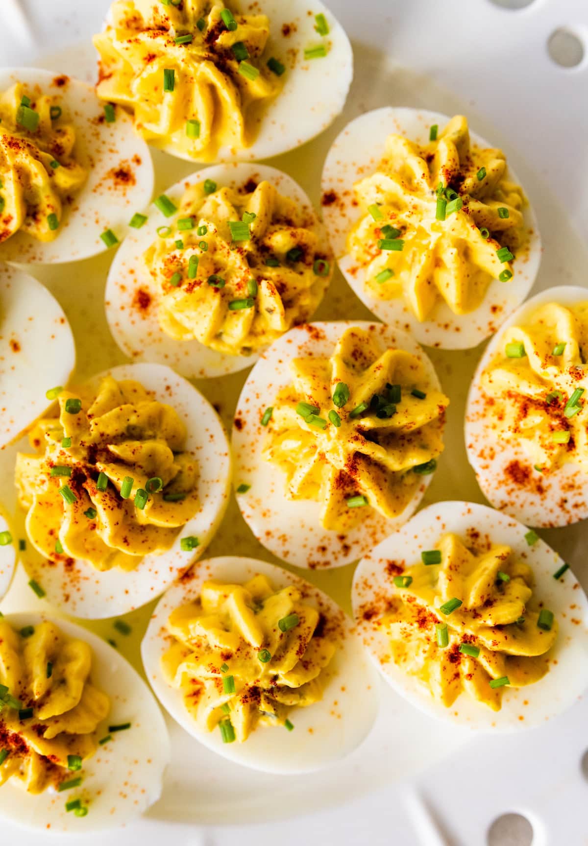 Deviled eggs topped with fresh chives, and paprika on a plate.