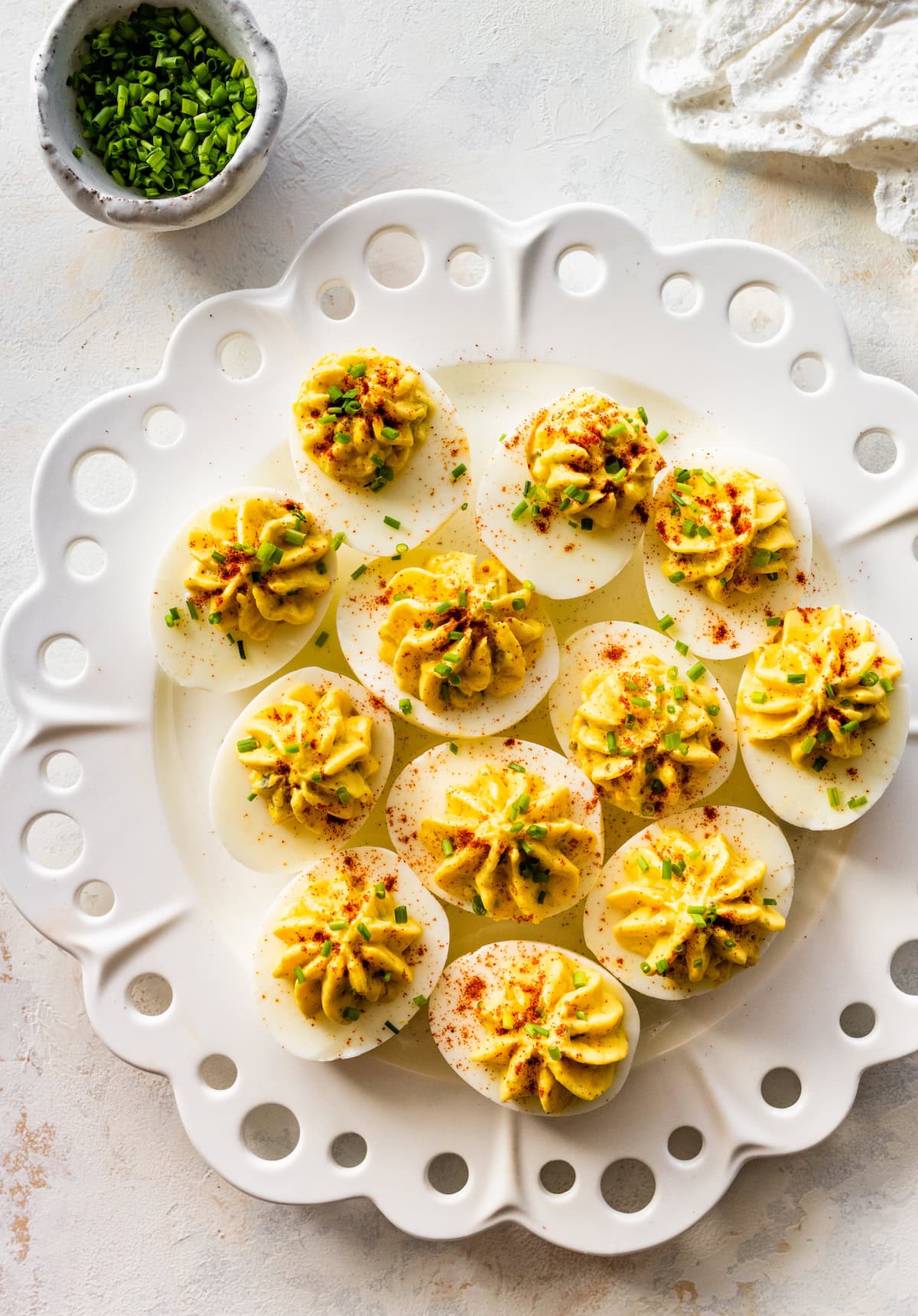 Deviled eggs presented on a plate topped with fresh chives and paprika.