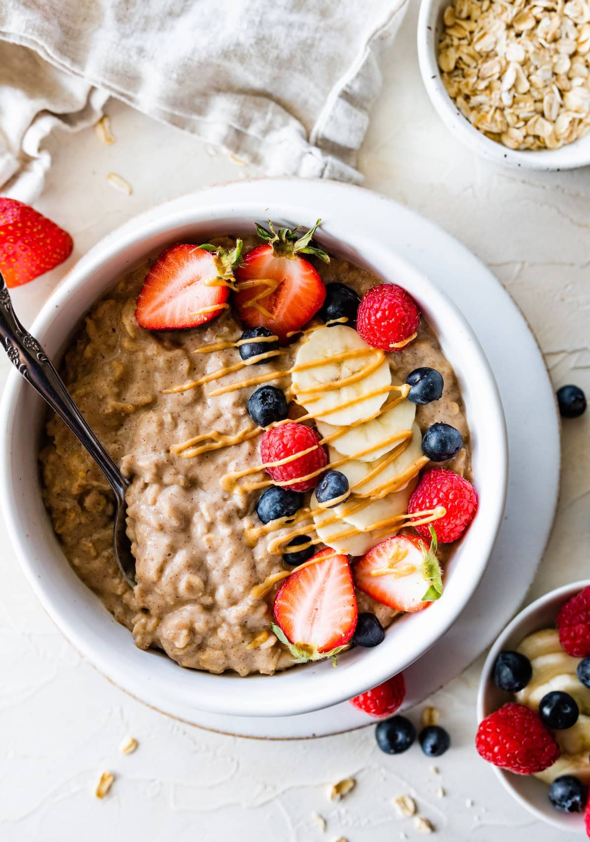 A serving of protein oatmeal in a bowl topped with fresh berries, banana, and a drizzle of peanut butter.