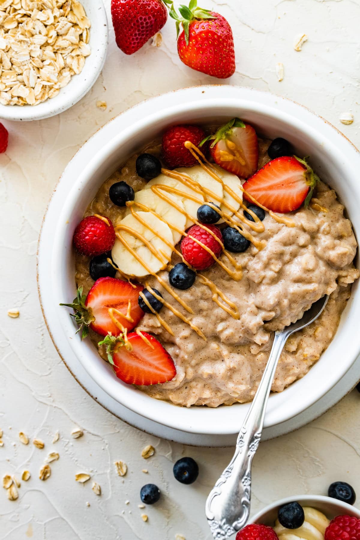 A white bowl with protein oatmeal topped with fresh berries, sliced banana, and a drizzle of peanut butter.