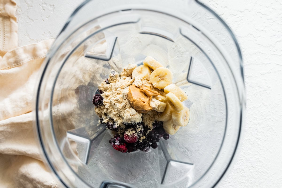 A blender with protein powder, nut butter, banana, and berries.