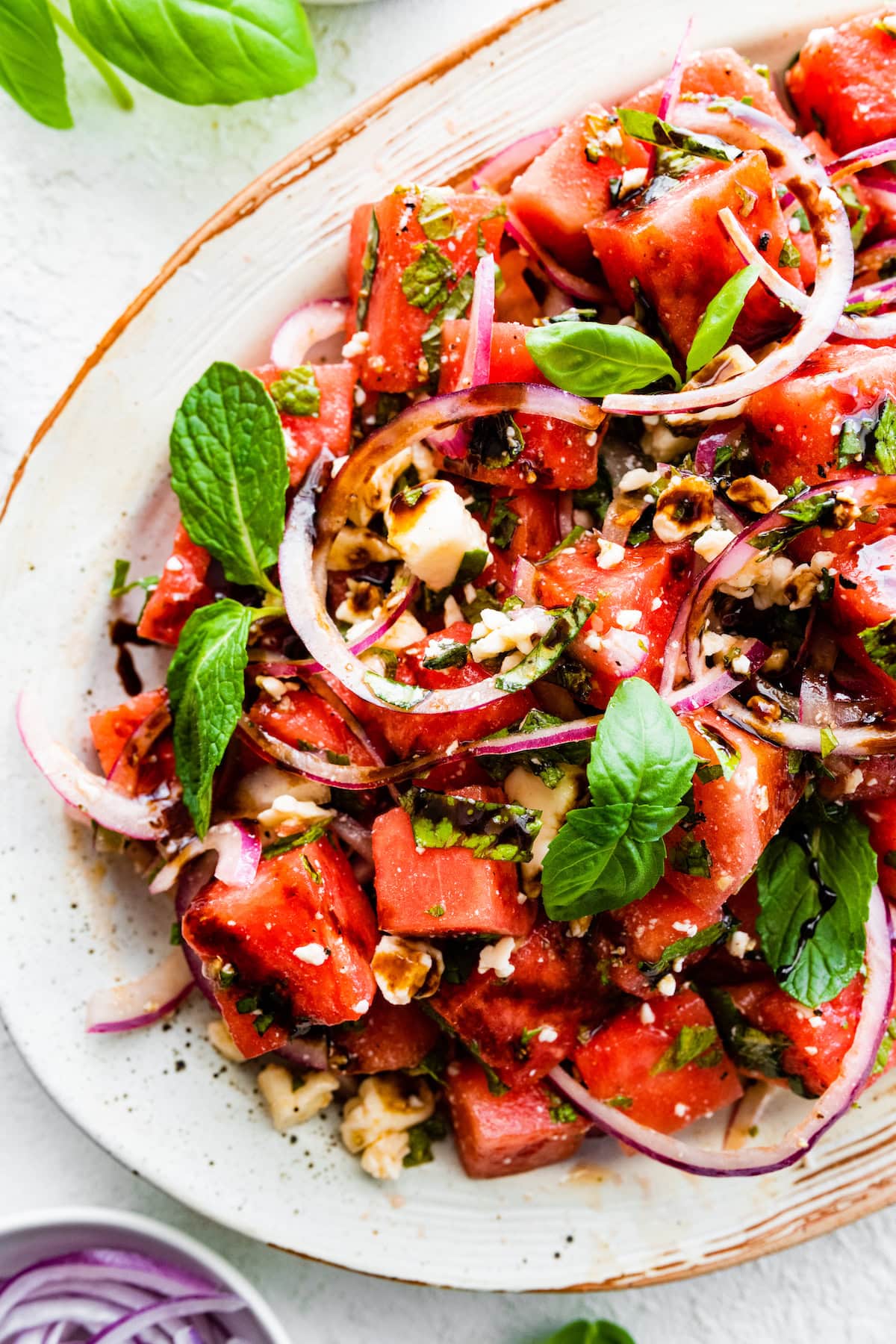 A large bowl with watermelon, feta cheese, red onion, balsamic vinegar, and fresh basil leaves.