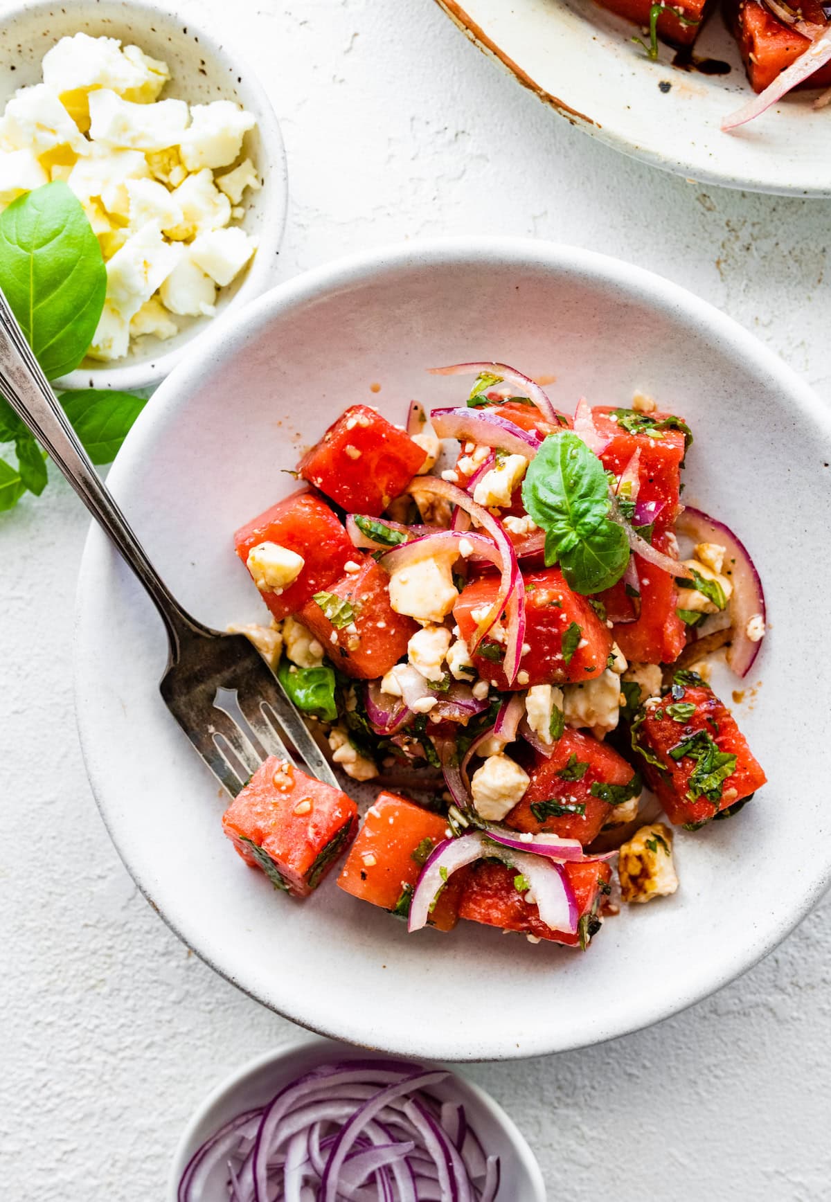 A serving of watermelon salad in a small bowl topped with feta cheese and fresh herbs.