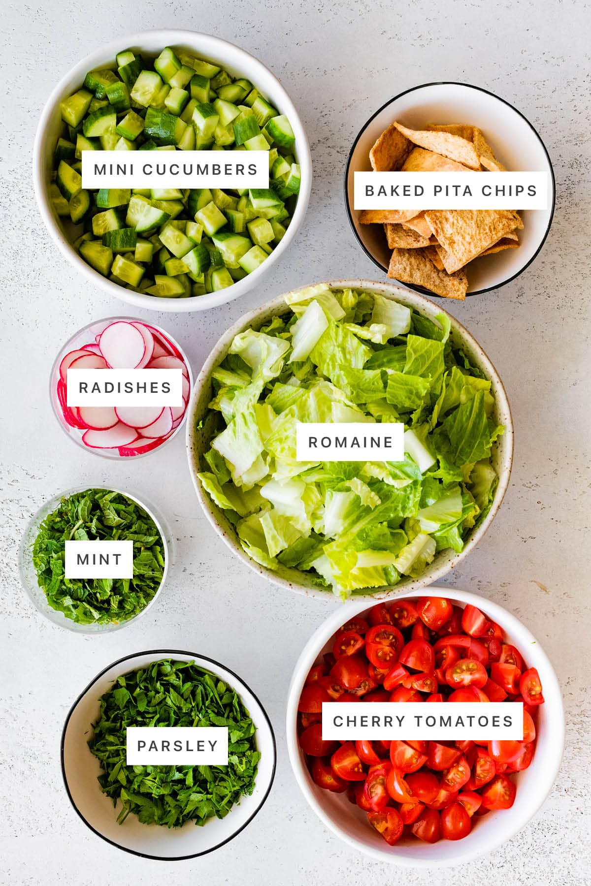 Ingredients measured out to make Fattoush Salad: mini cucumbers, baked pita chips, radishes, romaine, mint, parsley, cherry tomatoes.