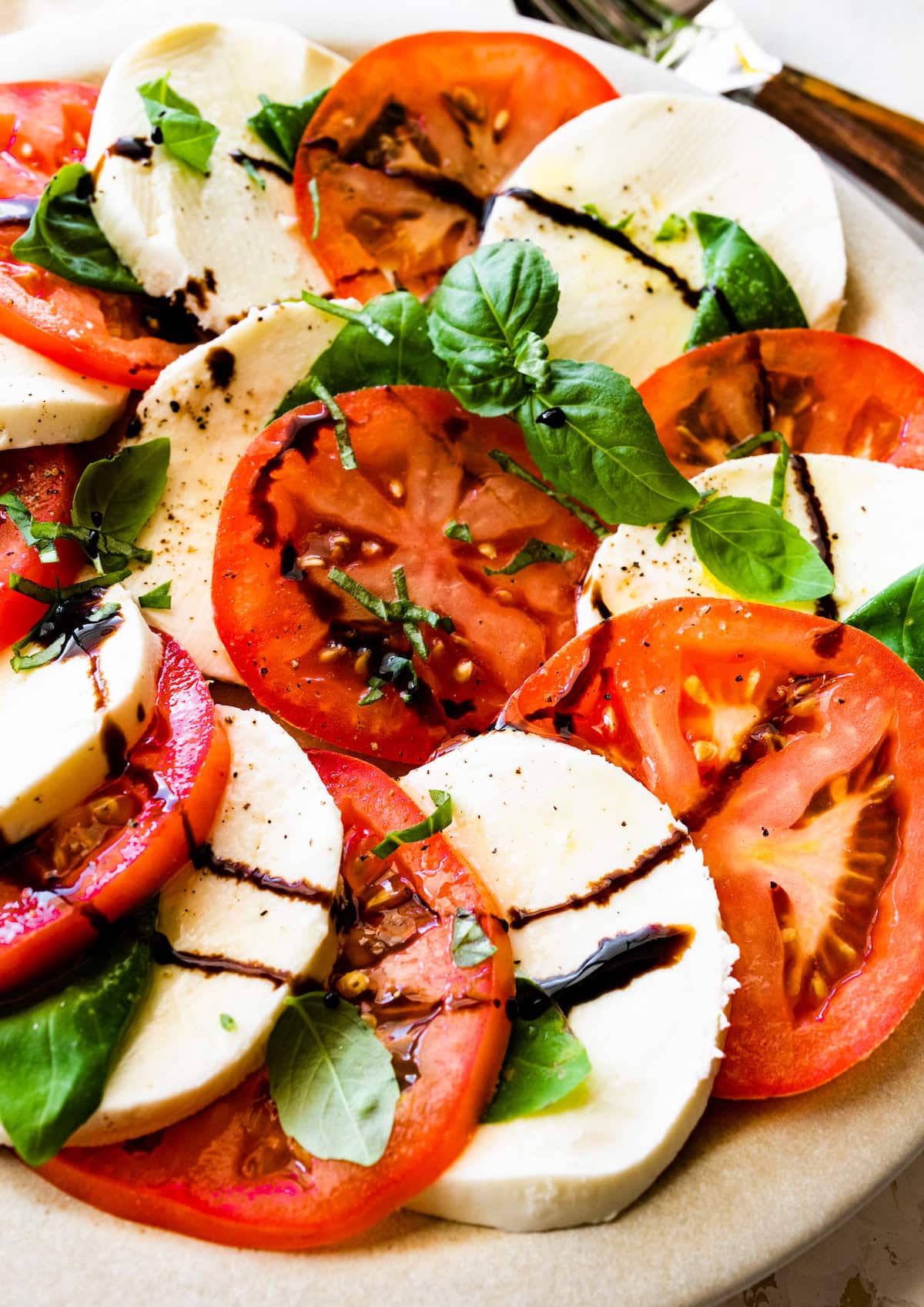 A large plate of a caprese salad with tomatoes, mozzarella cheese, fresh basil, and balsamic vinegar.