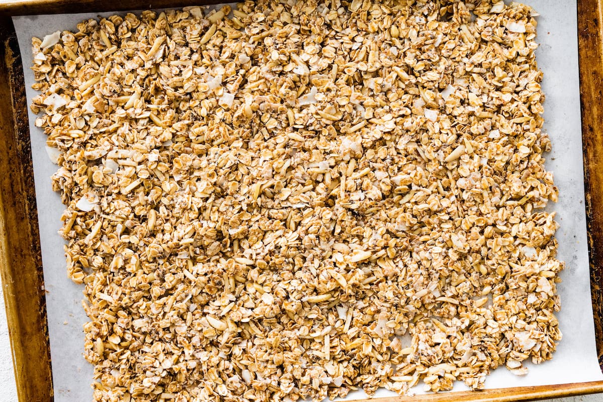 A large baking tray with coconut granola spread out on it before being baked.