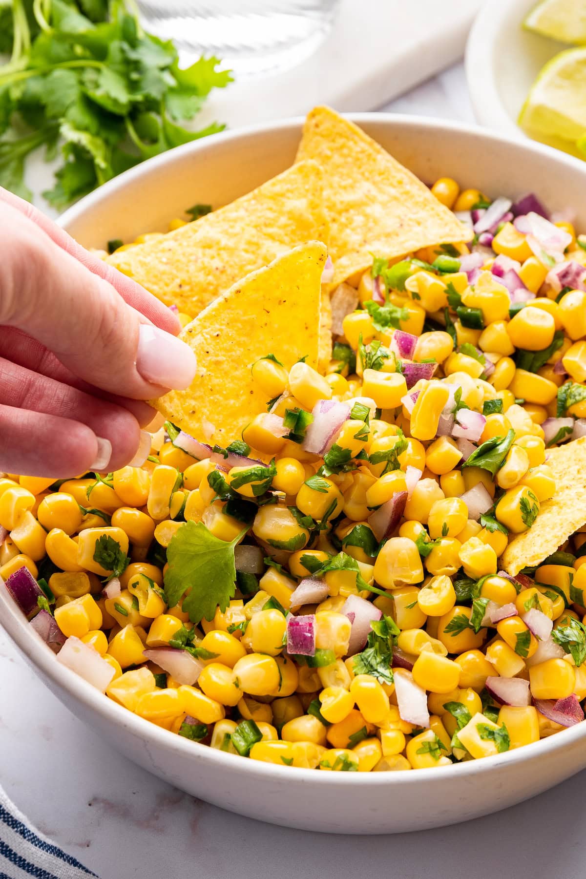A woman's hand dipping a tortilla chip in the corn salsa, which is corn mixed with red onion, cilantro and jalapeño.