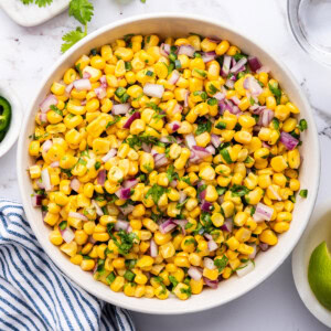 Corn mixed with red onion, cilantro and jalapeño in a white serving bowl.