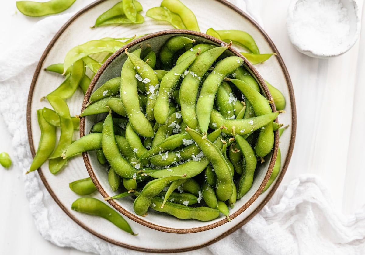 Cooked edamame pods with flaked sea salt in a white bowl.