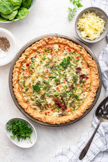 An unsliced cooked egg white quiche in a metal pie dish. Quiche is topped with fresh herbs.