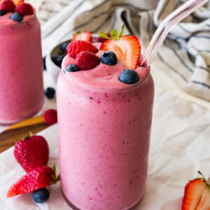 Two glasses filled with the berry kefir smoothie topped with fresh blueberries, raspberries and strawberries.