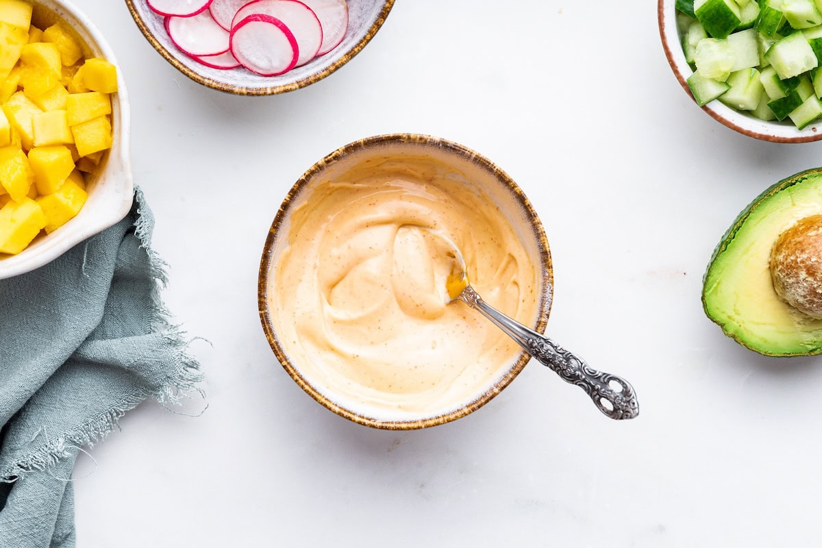A small bowl with a mayo mixture with a small metal spoon.