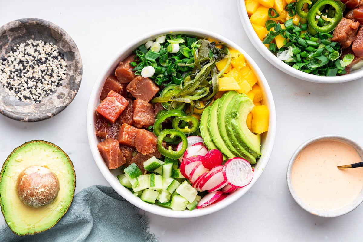 A serving of a poke bowl with tuna, jalapeño, cucumber, avocado, yellow onion, radish, and green onion.