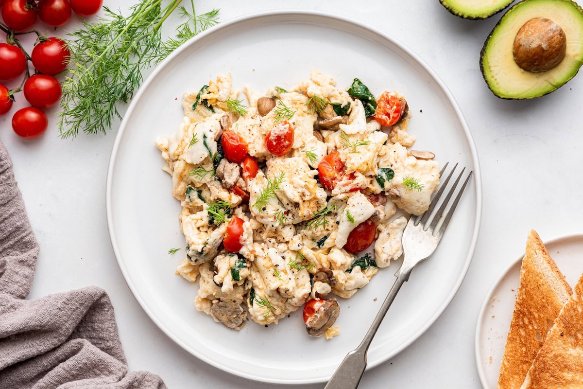 A serving of scrambled egg whites with cherry tomatoes and spinach on a plate with a metal fork.