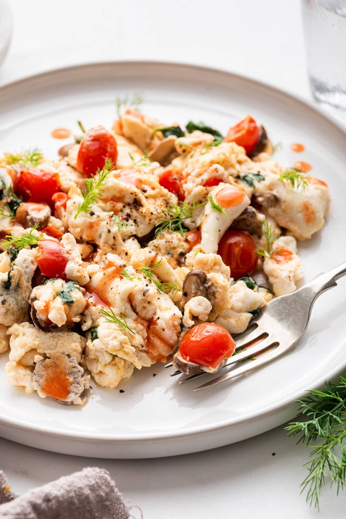 Scrambled egg whites with cherry tomatoes on a plate with a metal fork.