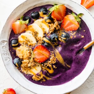 A smoothie bowl topped with fresh fruit, granola, and a drizzle of almond butter.