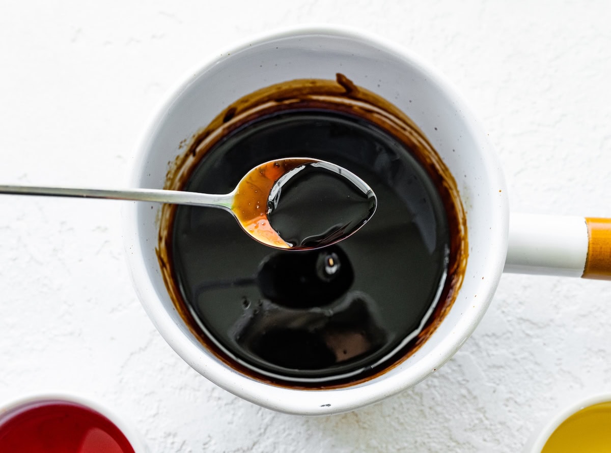 A balsamic reduction in a spoon over a saucepan.