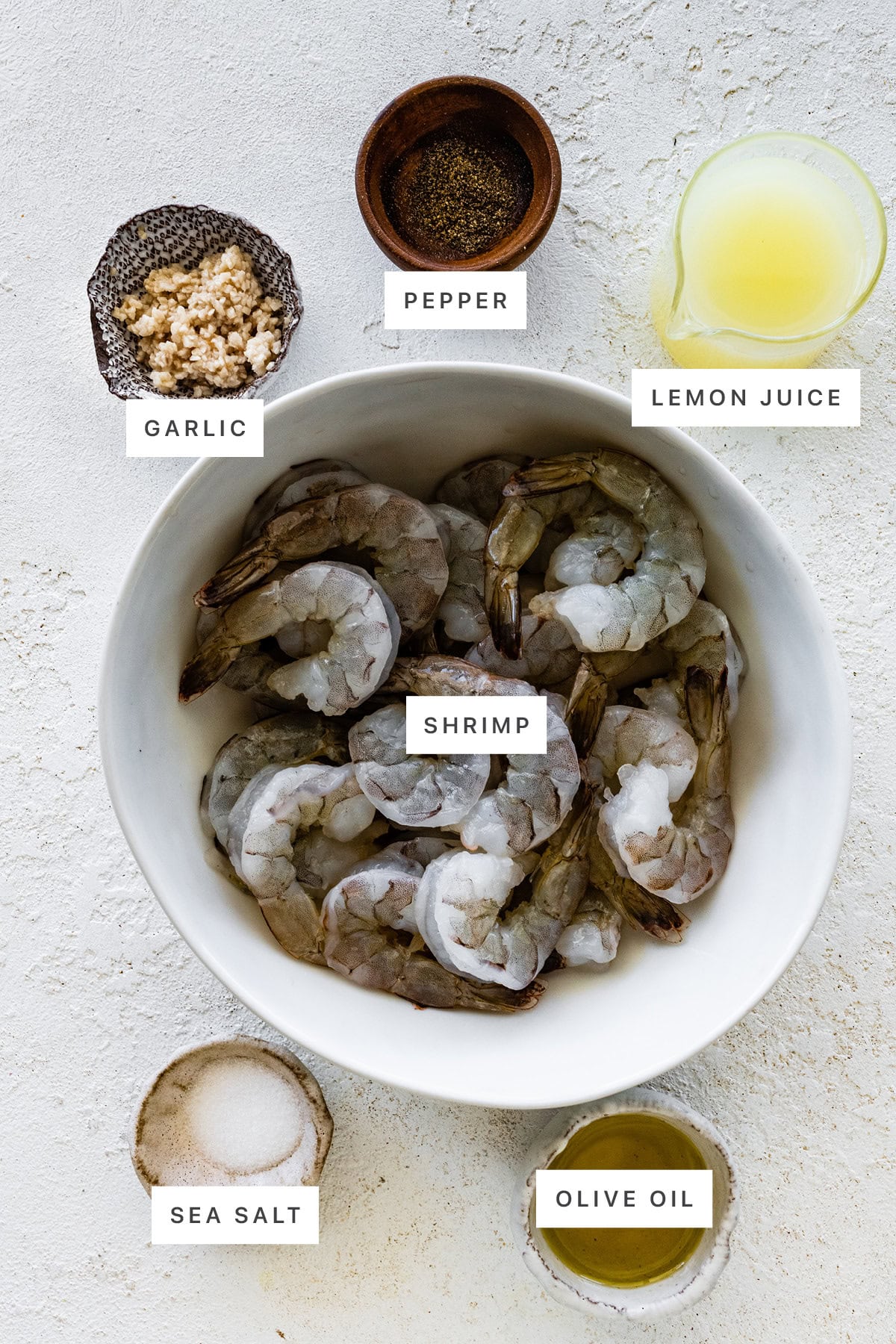 Ingredients measured out to make Grilled Shrimp Skewers: garlic, pepper, lemon juice, shrimp, sea salt and olive oil.