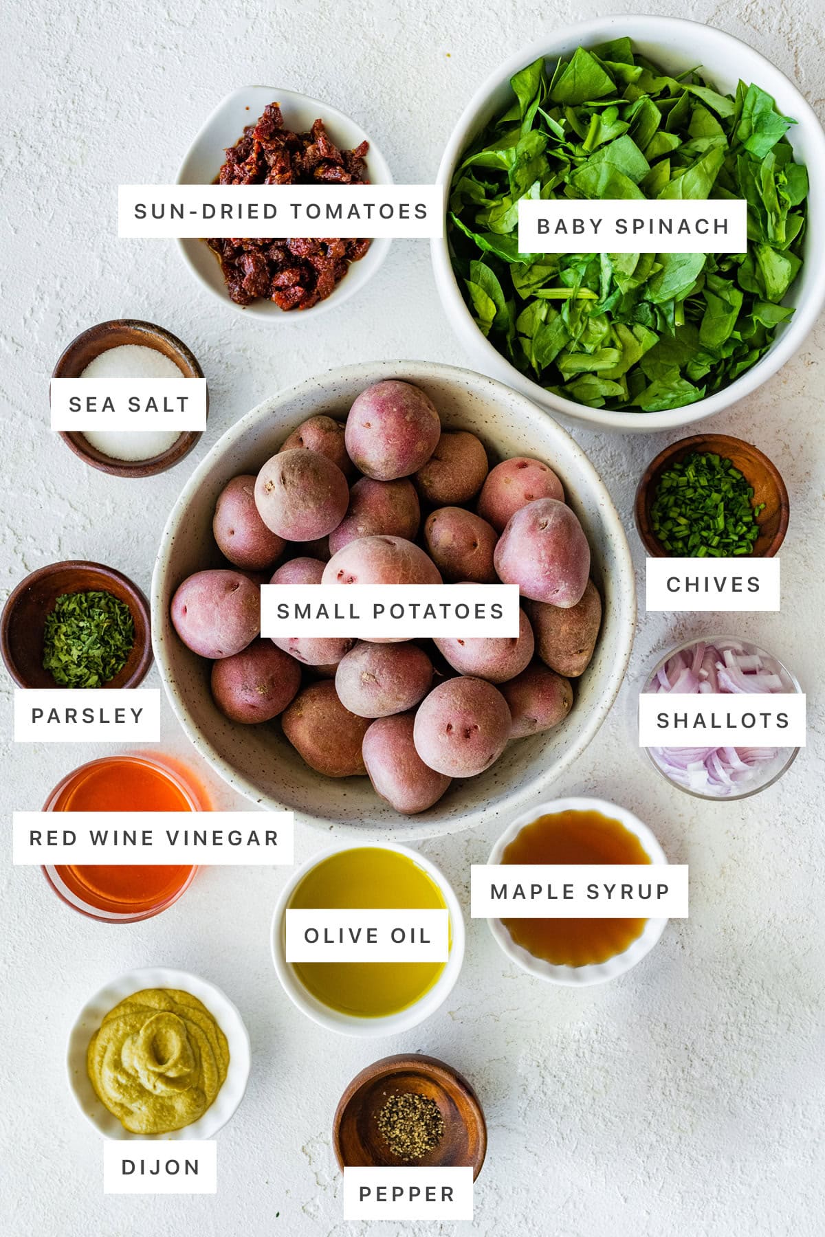 Ingredients measured out to make No Mayo Potato Salad: sun-dried tomatoes, baby spinach, sea salt, small potatoes, chives, parsley, shallots, red wine vinegar, olive oil, maple syrup, dijon and pepper.