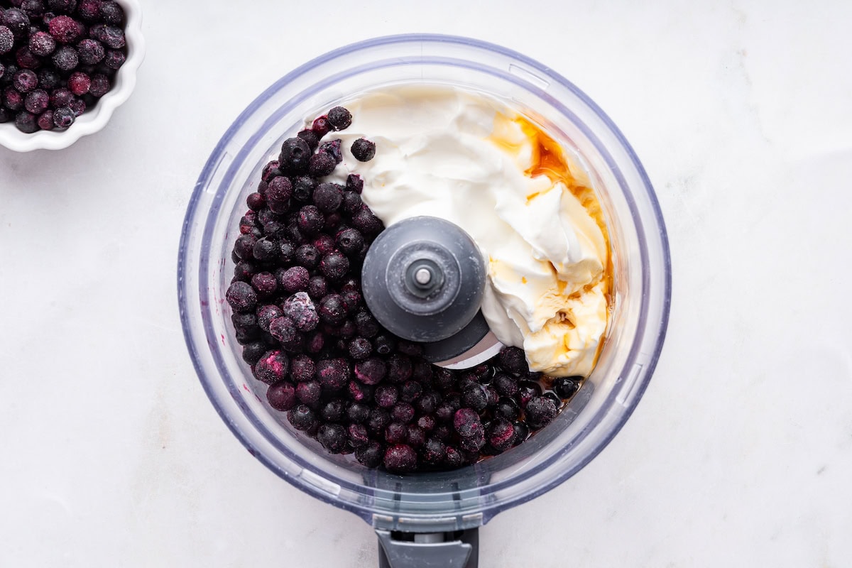 Frozen blueberries, yogurt, and maple syrup in a food processor.