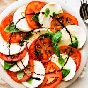A large plate of a caprese salad with sliced mozzarella cheese, tomatoes, fresh basil, and a drizzle of balsamic vinegar.