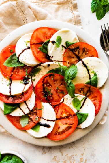 A large plate of a caprese salad with sliced mozzarella cheese, tomatoes, fresh basil, and a drizzle of balsamic vinegar.