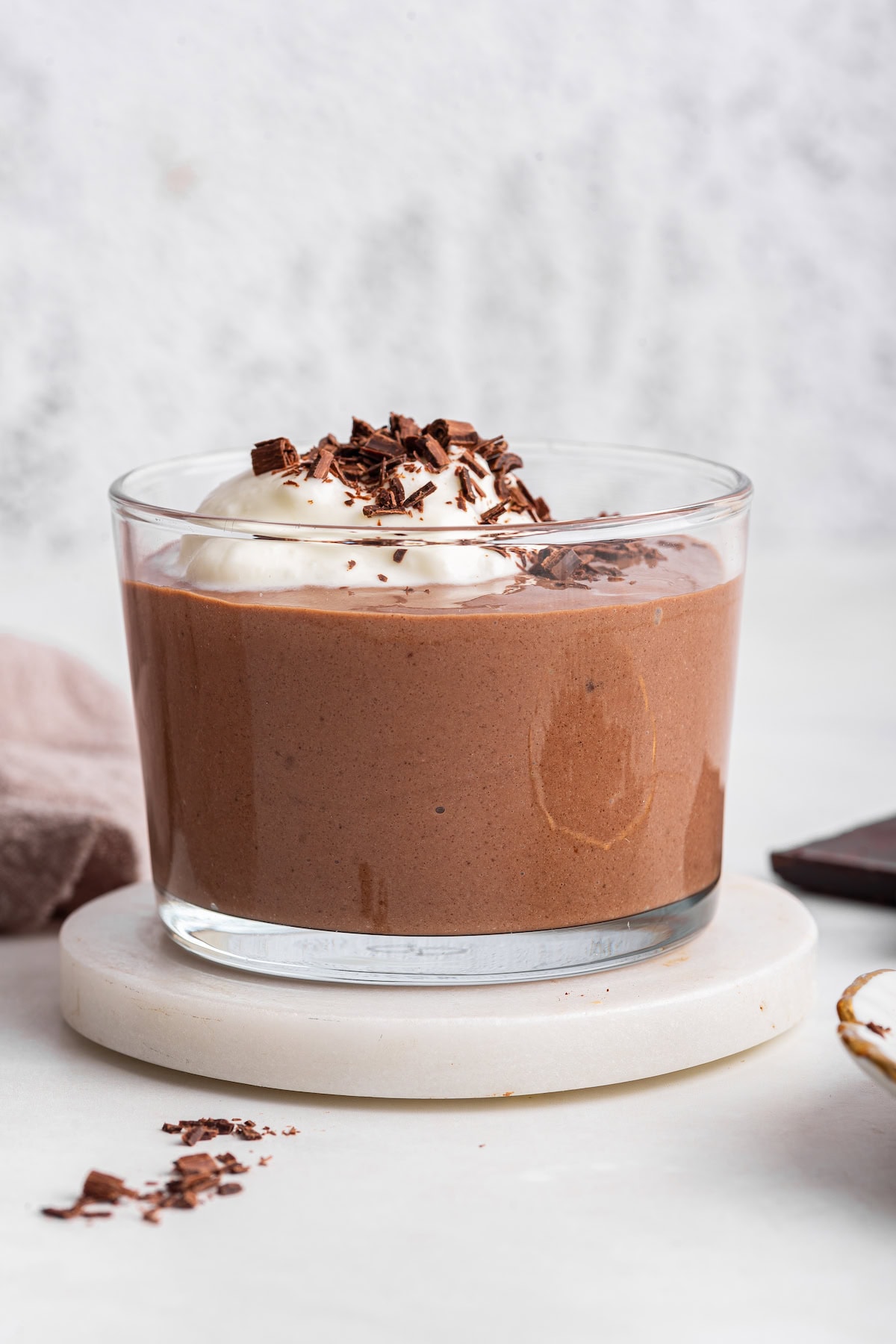 A glass cup of chocolate pudding made with cottage cheese, topped with shaved chocolate and whipped cream.