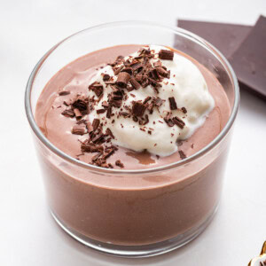 A chocolate protein pudding made with cottage cheese in a glass cup topped with whipped cream and shaved chocolate.