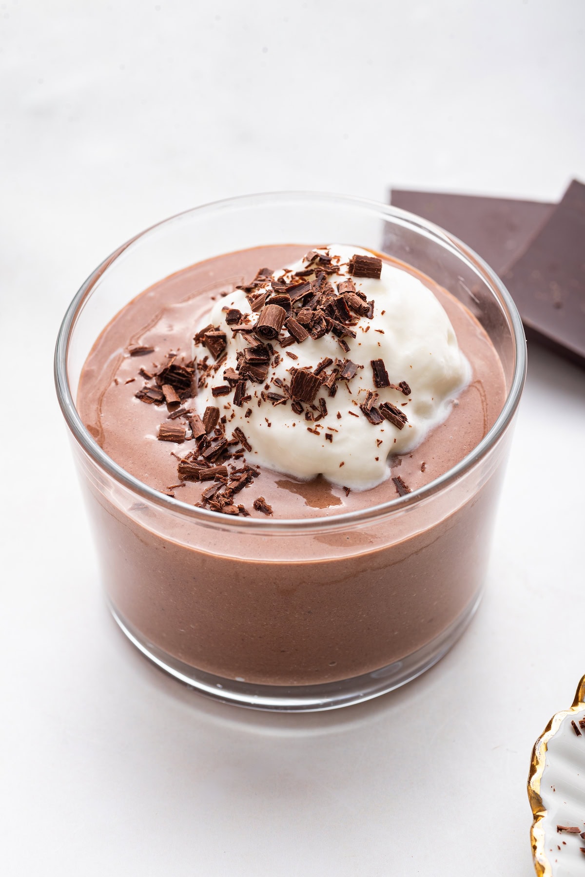A chocolate protein pudding made with cottage cheese in a glass cup topped with whipped cream and shaved chocolate.