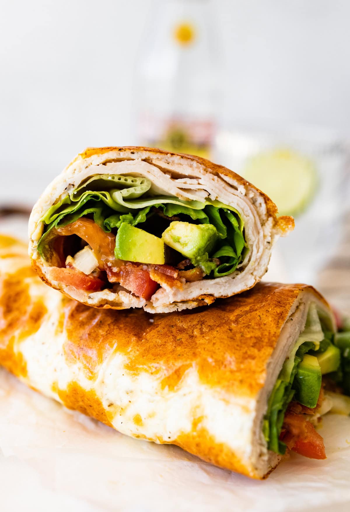Two sections of a cottage cheese wrap with turkey, tomato, avocado, lettuce and onion visible inside the wrap.