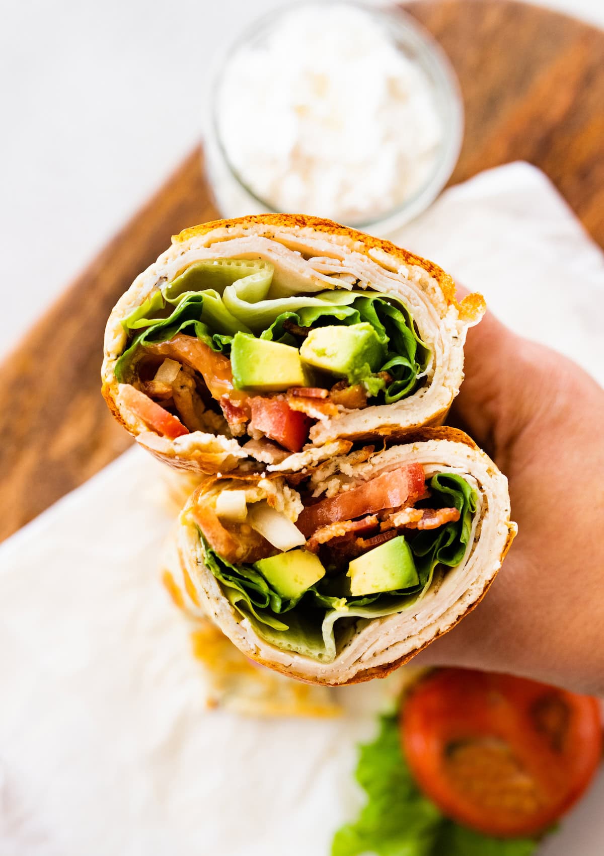 A woman's hand holding two sections of a cottage cheese wrap with turkey, tomato, avocado, lettuce and onion visible inside the wrap.
