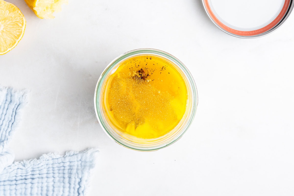 A glass jar with dijon mustard, vinegar, and lemon juice before being mixed.