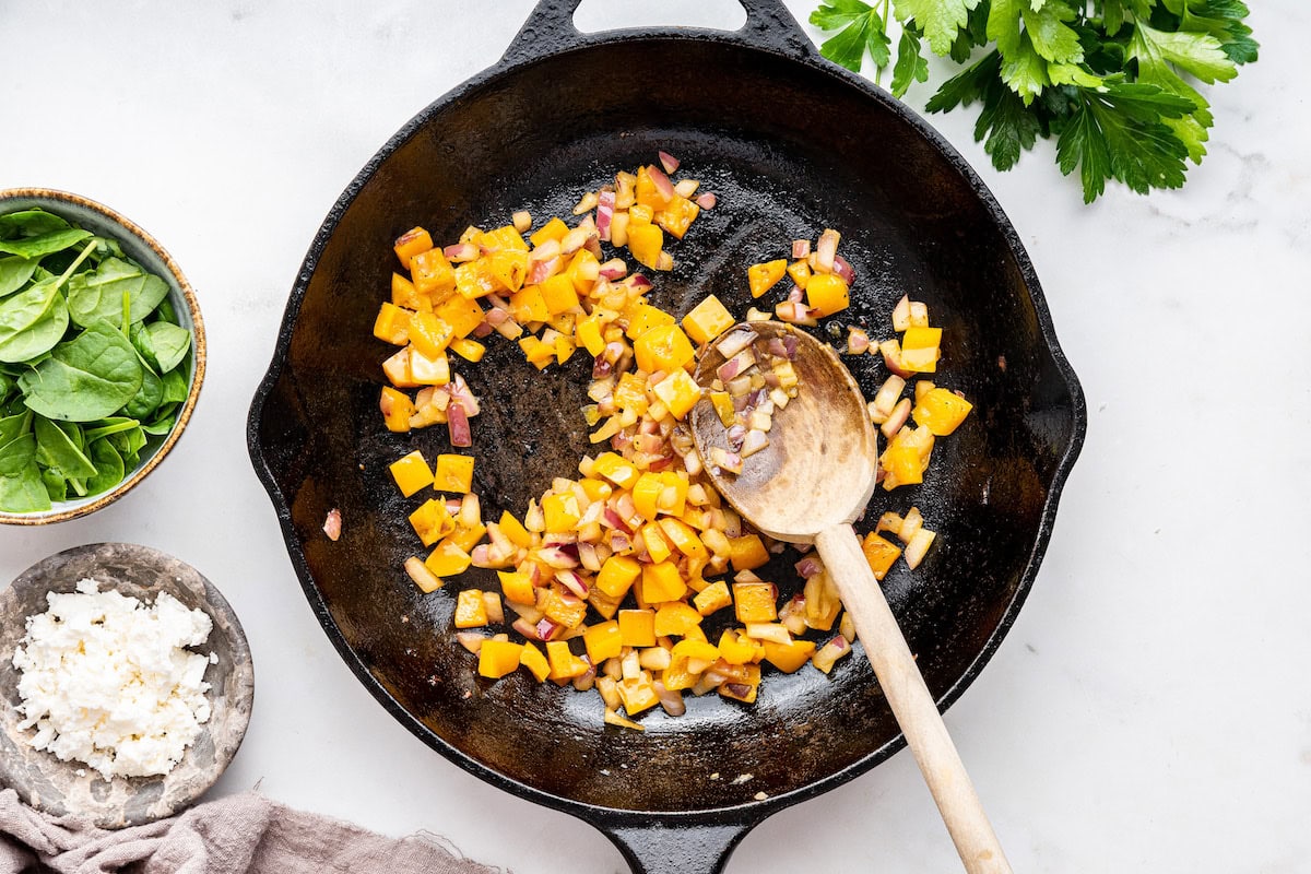 Sauteed orange bell pepper and red onion in a cast iron skillet with a wooden spoon.