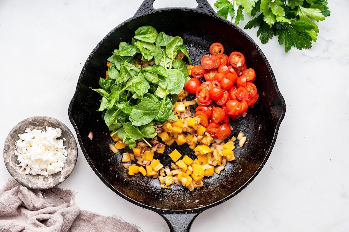 Cherry tomatoes and spinach are added to a cast iron skillet with sauteed bell pepper and red onion.